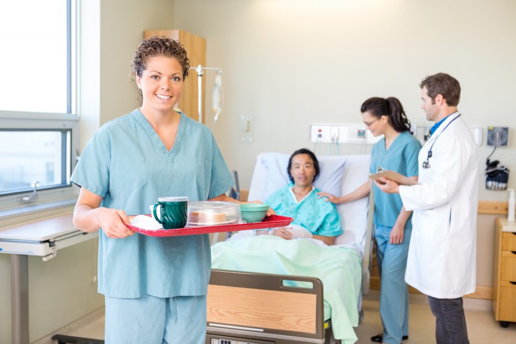 Nurse serving breakfast to a patient in a hospital room.
