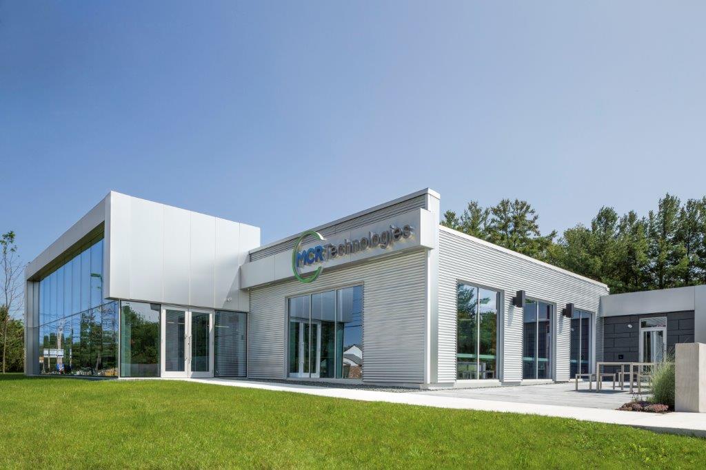 Modern white commercial building with large windows and green lawn.